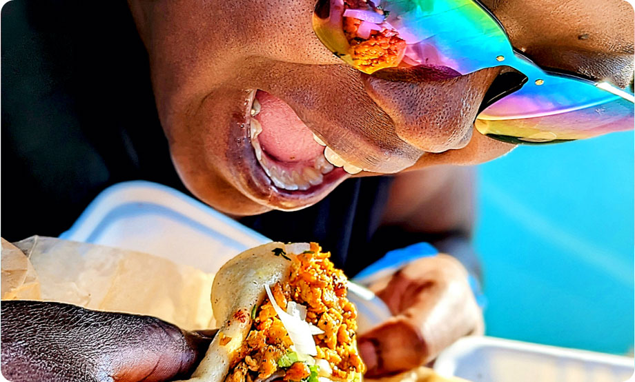 Closeup of woman with bright sunglasses bringing taco to her mouth to take a bite