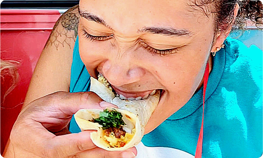 Closeup of woman with a taco in her hand and taking a big bite out of the taco