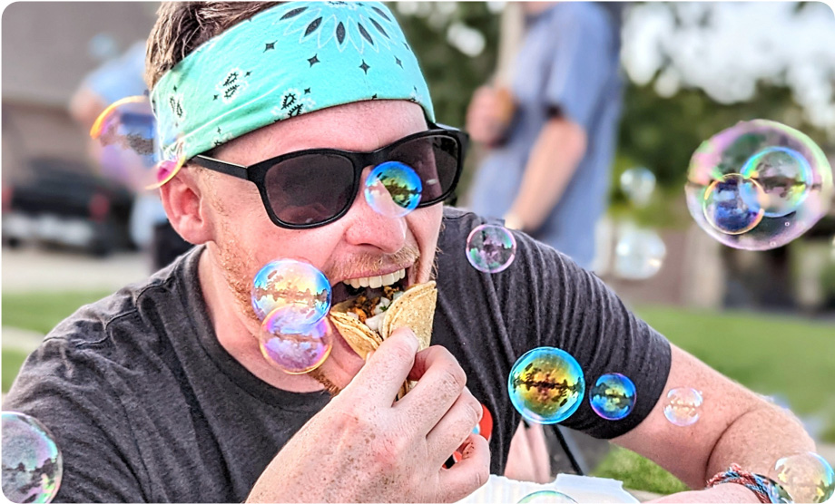 Man with a green bandana and black sunglasses eating a taco with bubbles around him
