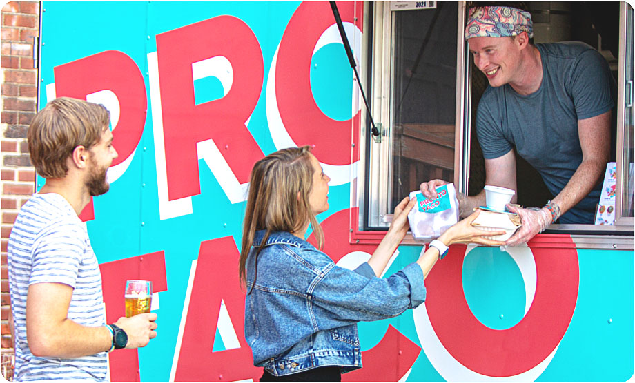 Man serving a woman tacos out of a food truck window