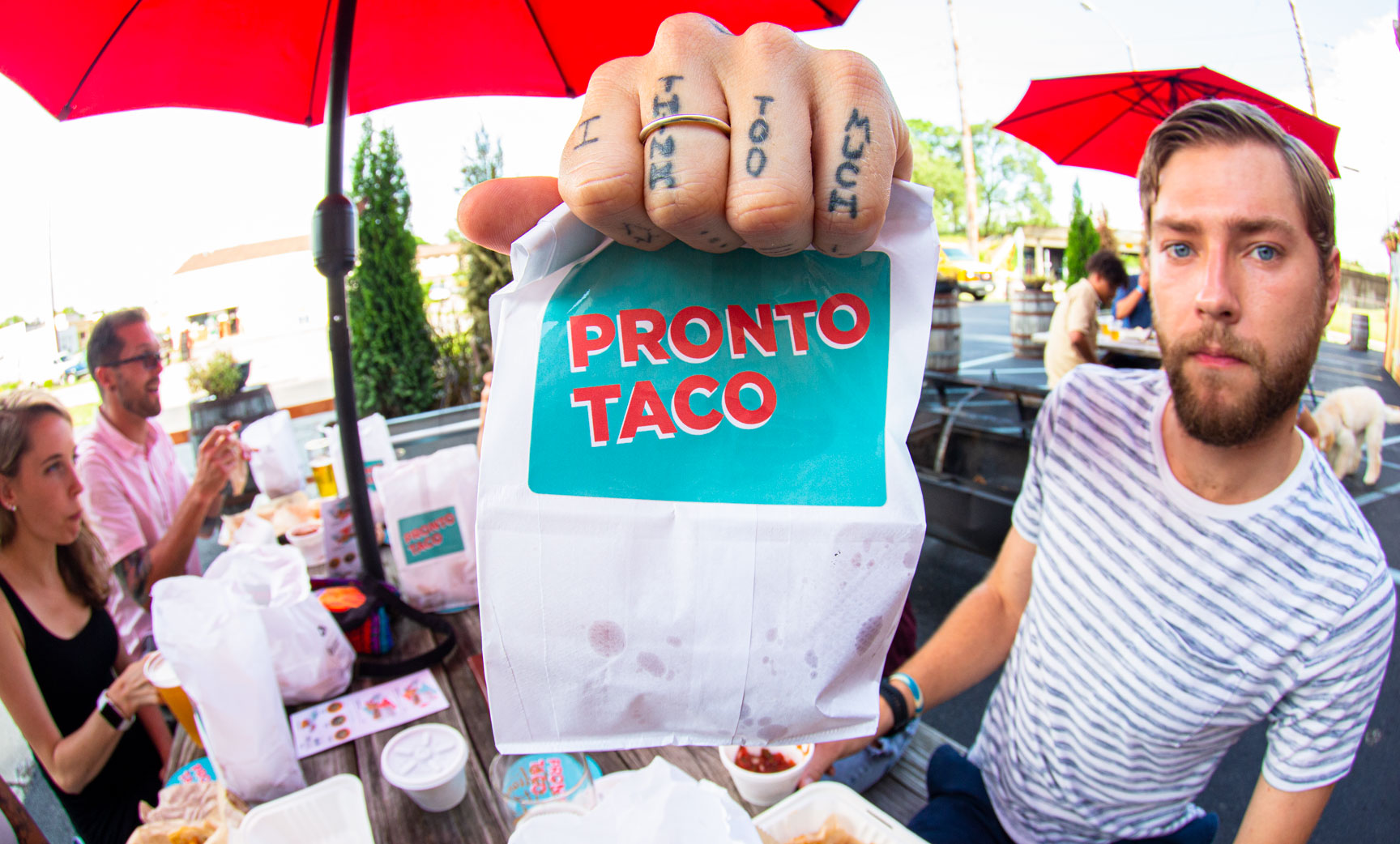 Fish eye lens photo of people eating Pronto Taco food at an outdoor table with Pronto Taco mobile kitchen in background