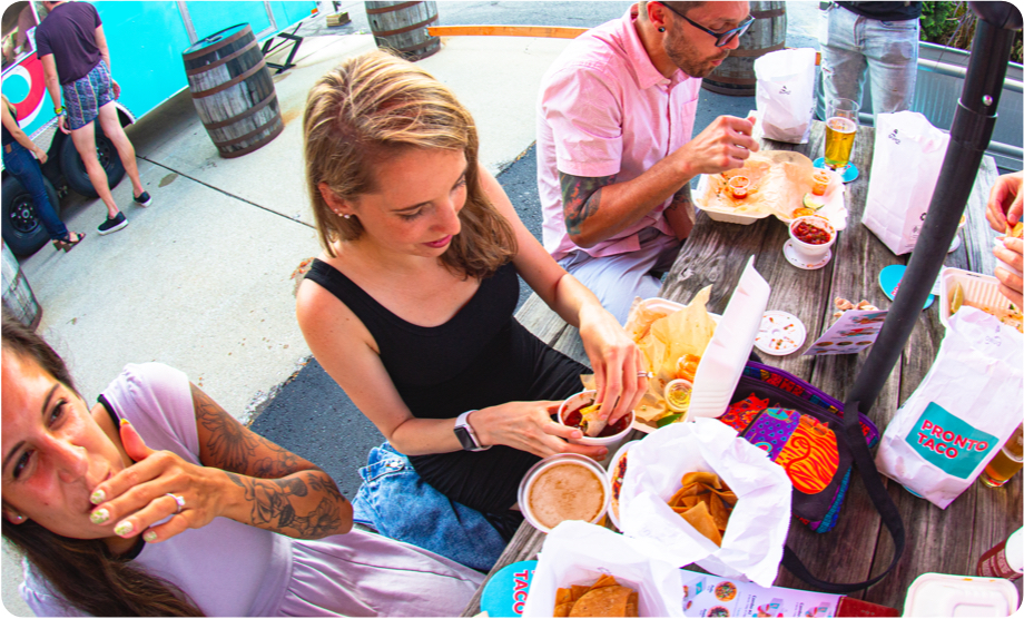 Smiling Pronto Taco man serving food to two smiling tattooed women