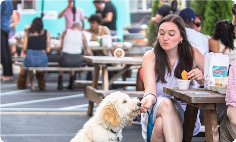 White woman with long brown hair giving a bite to her dog